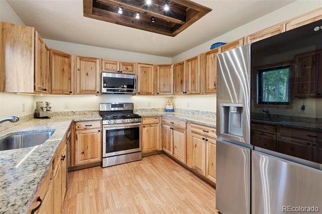 Kitchen with light wood cabinets, granite countertops, stainless steel appliances, and a ceiling skylight.
