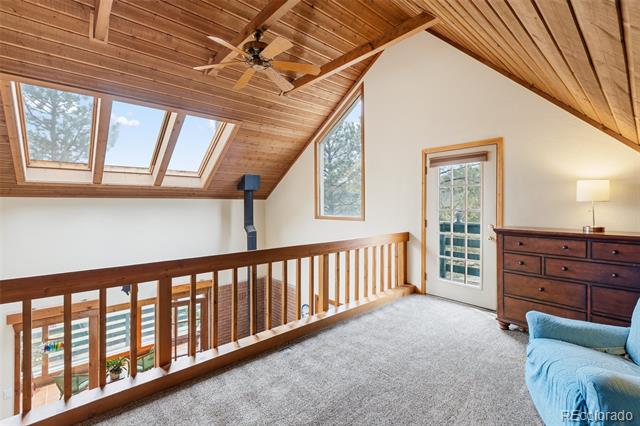 Furnished loft with a vaulted wood ceiling, skylights, and railing overlooking the level below.