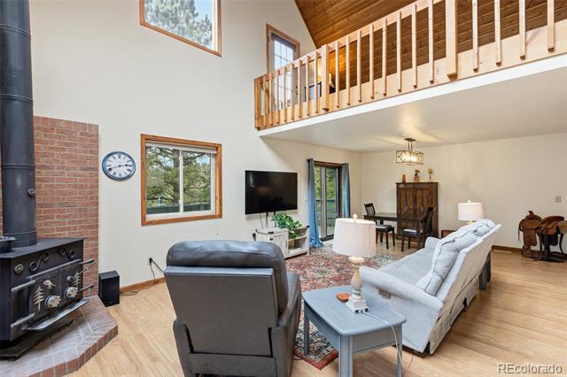 Furnished living room with a brick-hearth wood stove, vaulted wood ceiling, and upstairs balcony.