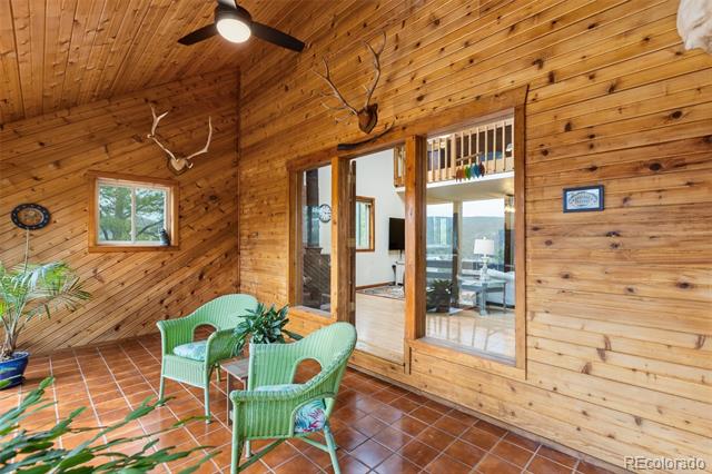 Wood-paneled sunroom with green wicker chairs, tiled floor, and glass doors.