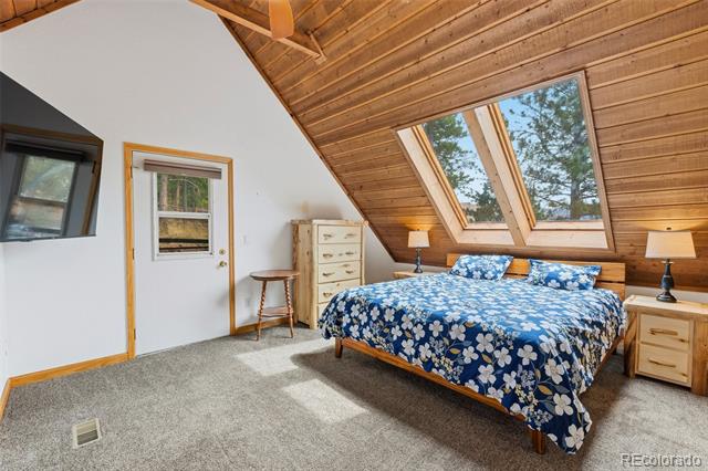 Bedroom with a blue floral bed beneath a sloped wood ceiling and skylights.