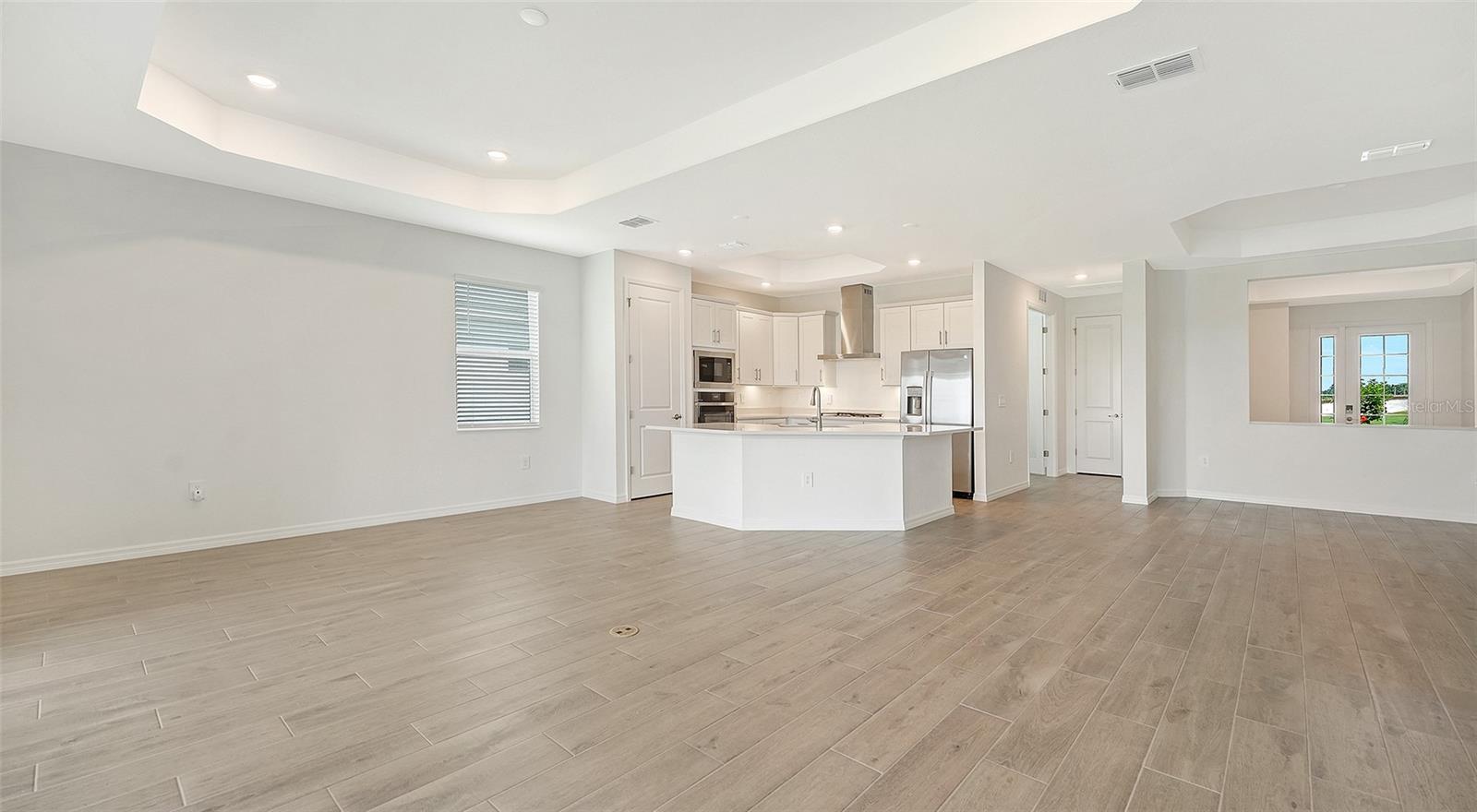 Open-plan kitchen and living area with a large island, stainless steel appliances, and light tile flooring.