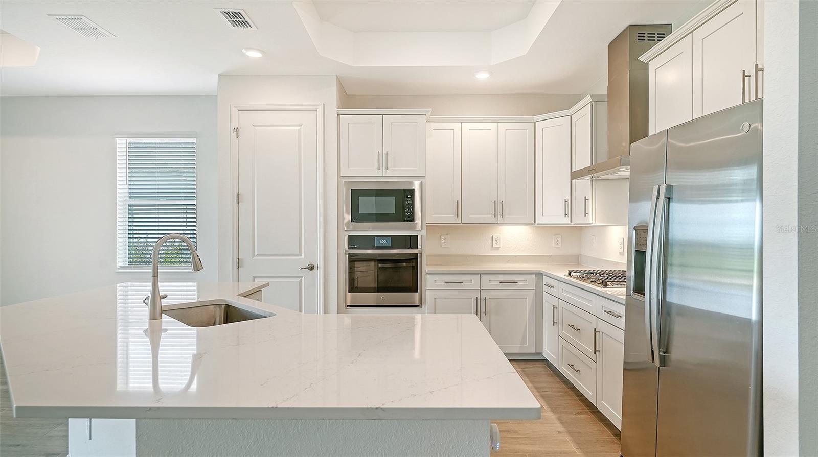 Modern white kitchen with a large veined island, gas cooktop, and stainless steel appliances.