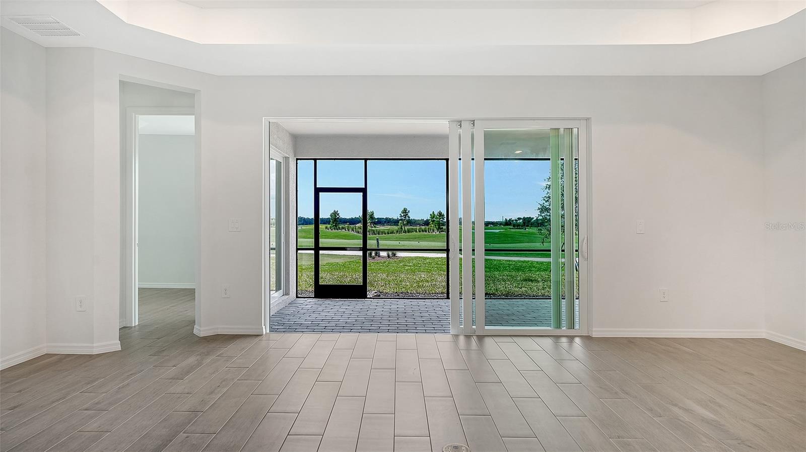 Vacant living room with tiled floors and sliding glass doors overlooking a golf course.
