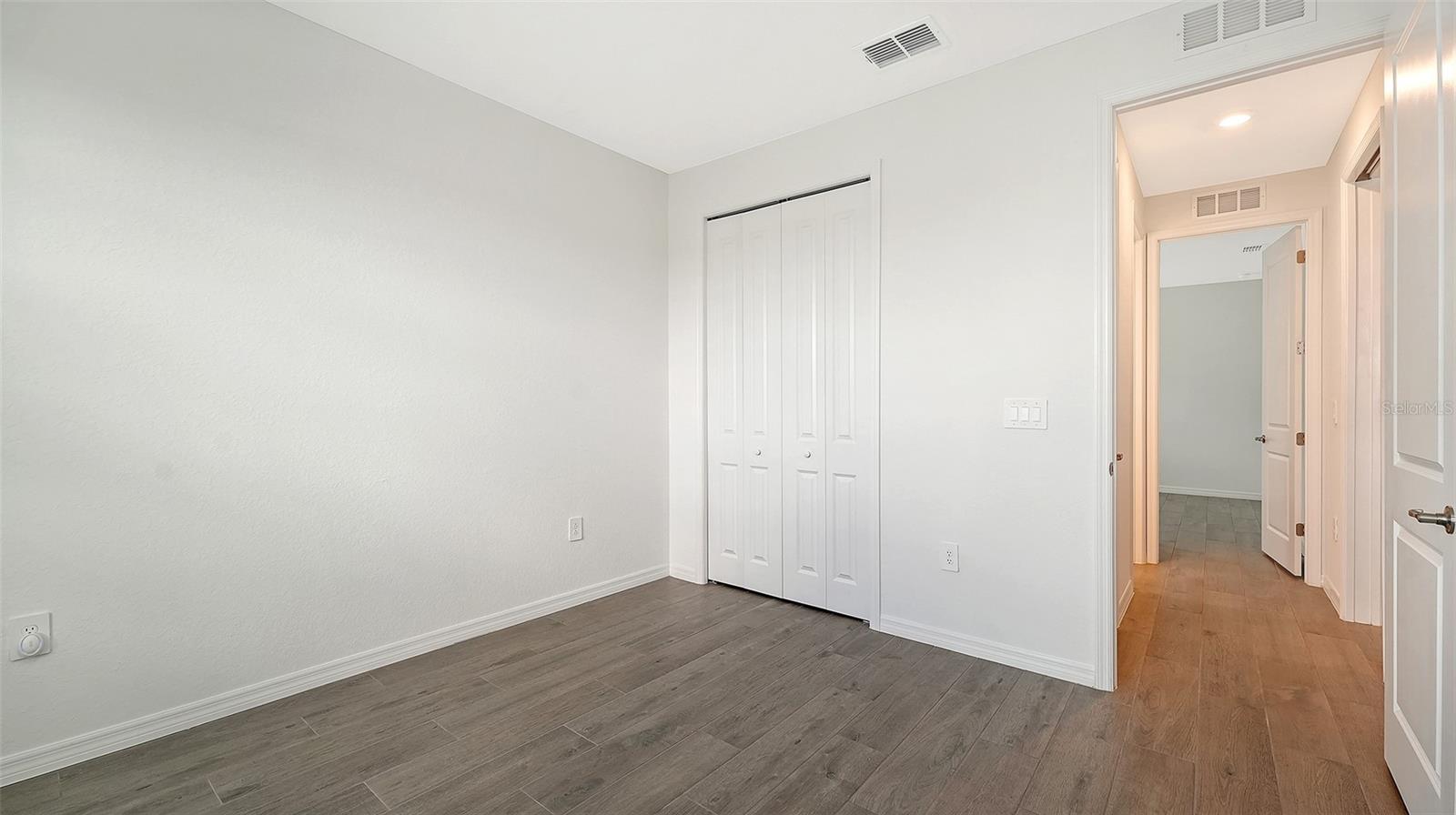 Empty bedroom with a double-door closet and gray wood-look tile flooring.