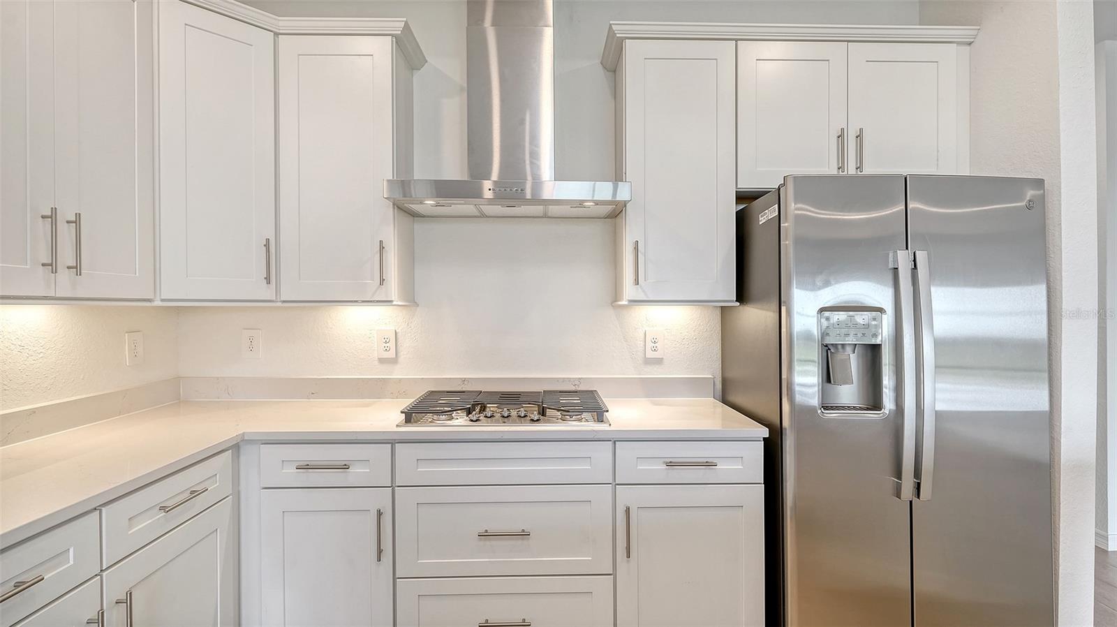 Kitchen with white cabinets, stone countertops, a gas cooktop, and stainless steel appliances.