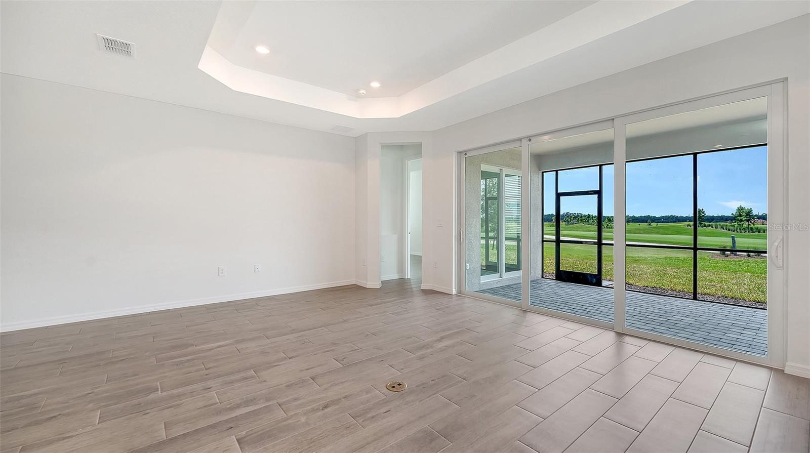 Empty tiled room with a tray ceiling and sliding doors overlooking a golf course.