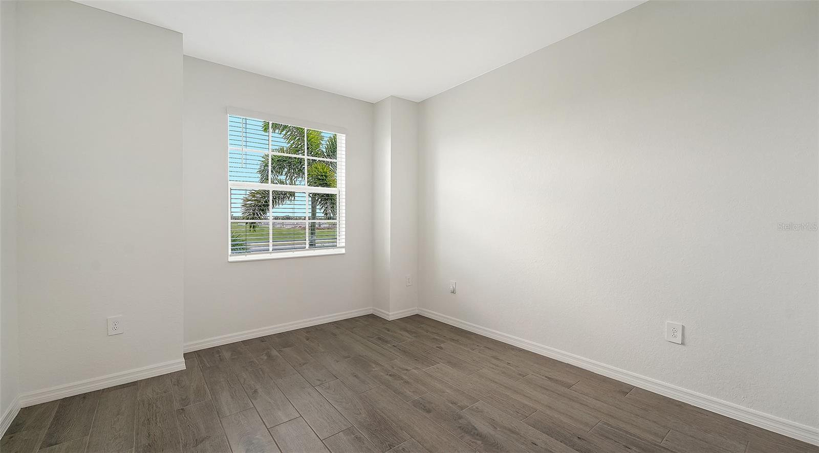 Unfurnished room with wood-look tile flooring and a window overlooking palm trees and lawn.