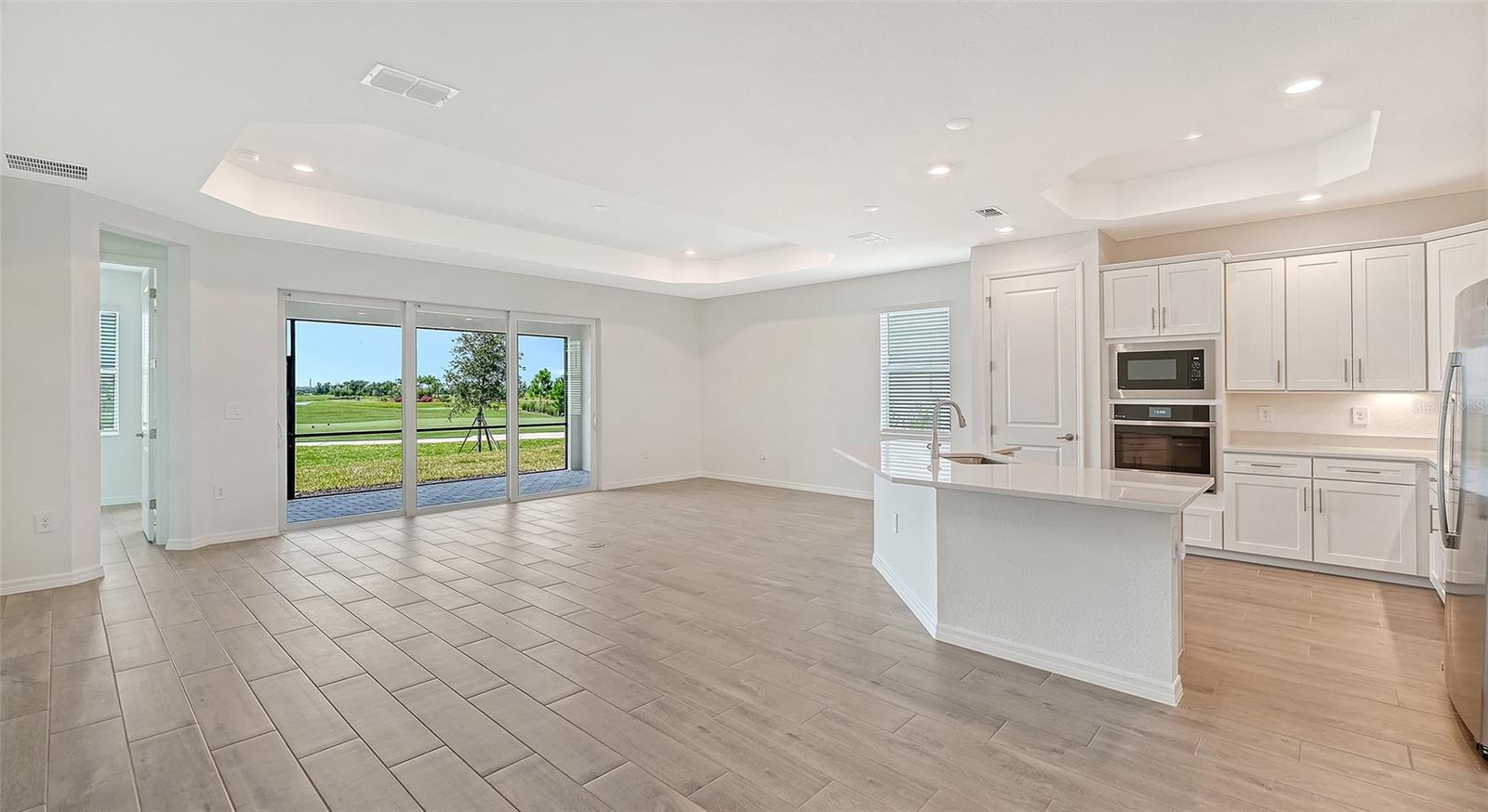 Open kitchen and living area with white cabinetry and sliding doors overlooking a golf course.