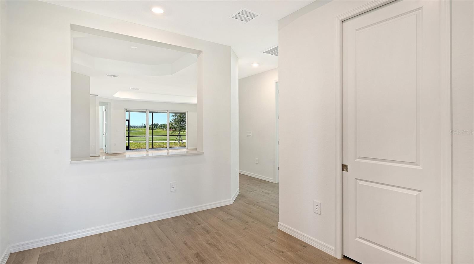 Vacant interior with light wood-look flooring and a wide opening toward sliding glass doors.