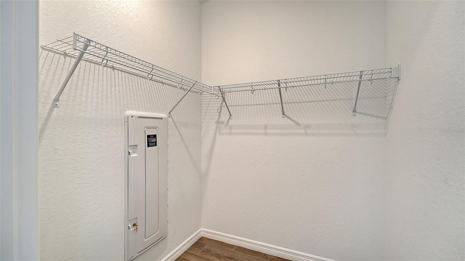 Empty closet with wraparound wire shelving and a wall-mounted electrical panel.