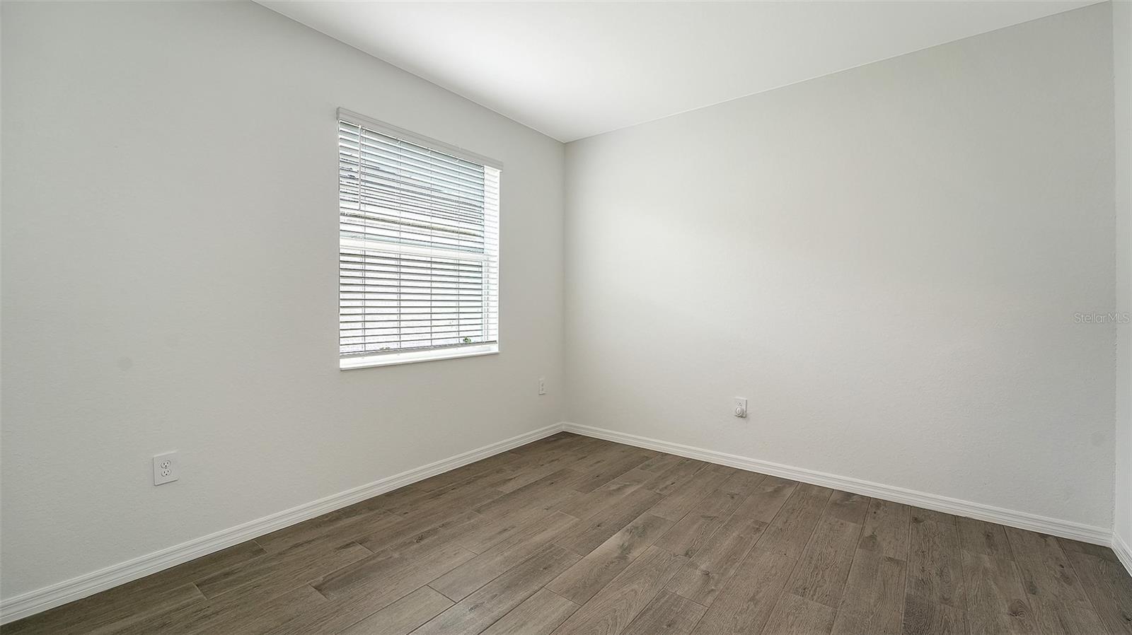 Empty bedroom with brown plank flooring and a window with blinds.