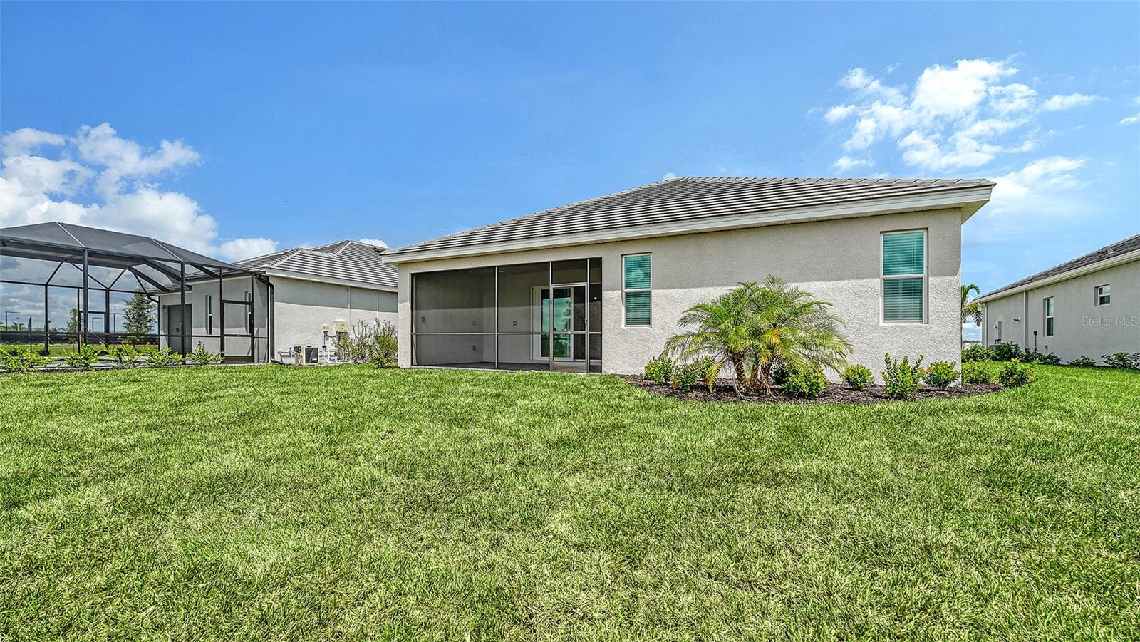 Rear of a single-story home with a screened lanai and wide green lawn.