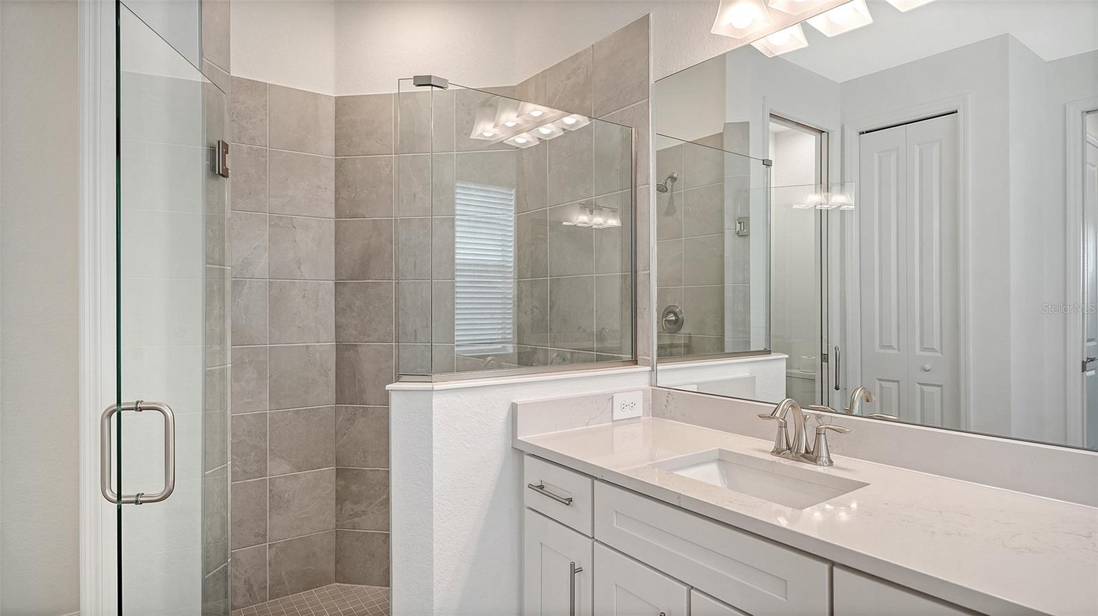 Bathroom with a tiled glass shower and white vanity beneath a large mirror.