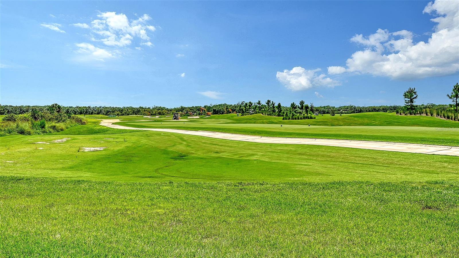 Expansive golf course with green fairways, a curving sand bunker, and a bright blue sky.