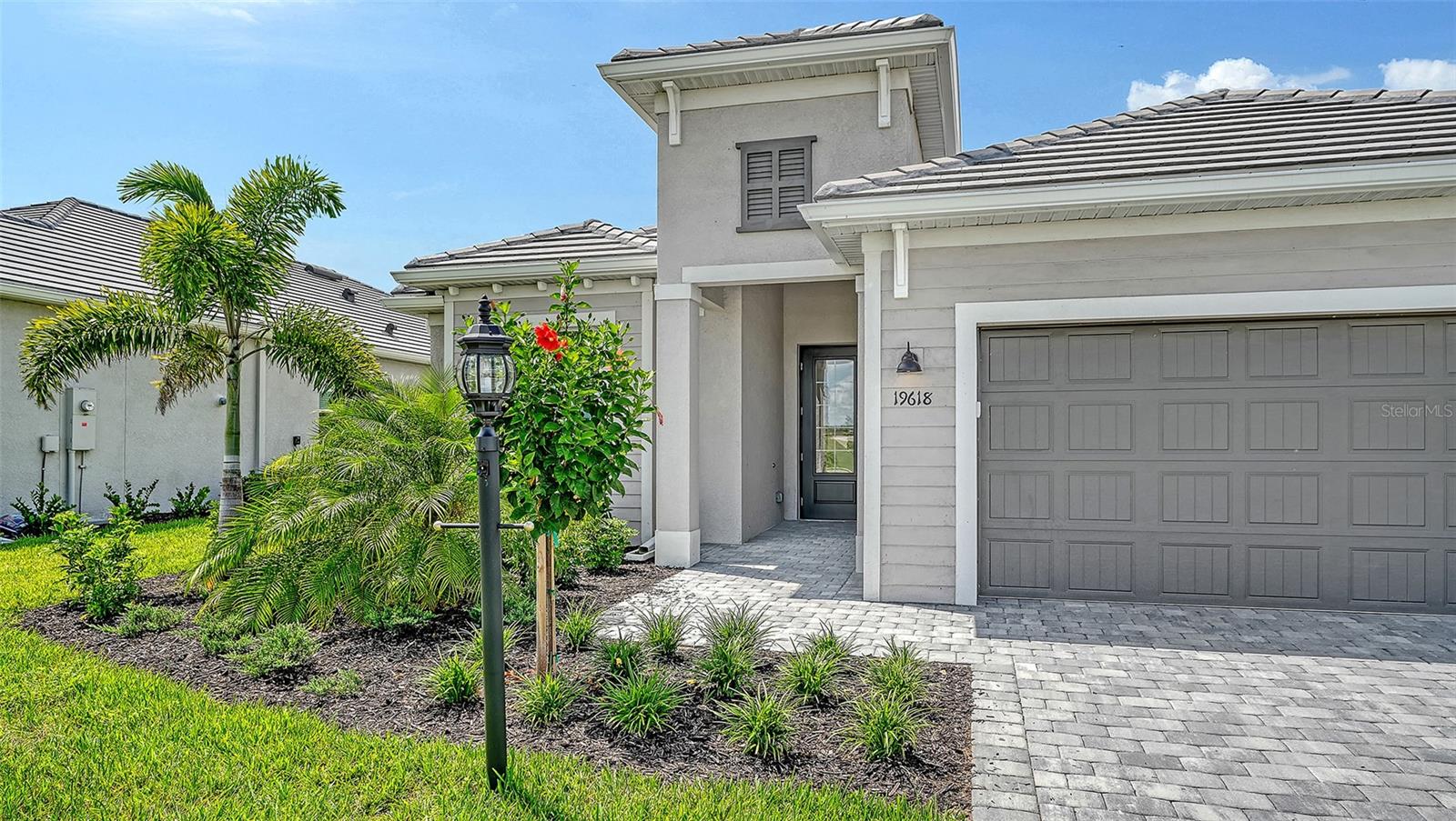 Gray two-story home with a large garage, paver driveway, and landscaped front yard.