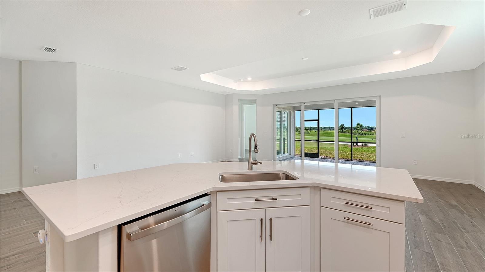 Vacant kitchen with a large white island and sliding doors overlooking a golf course.