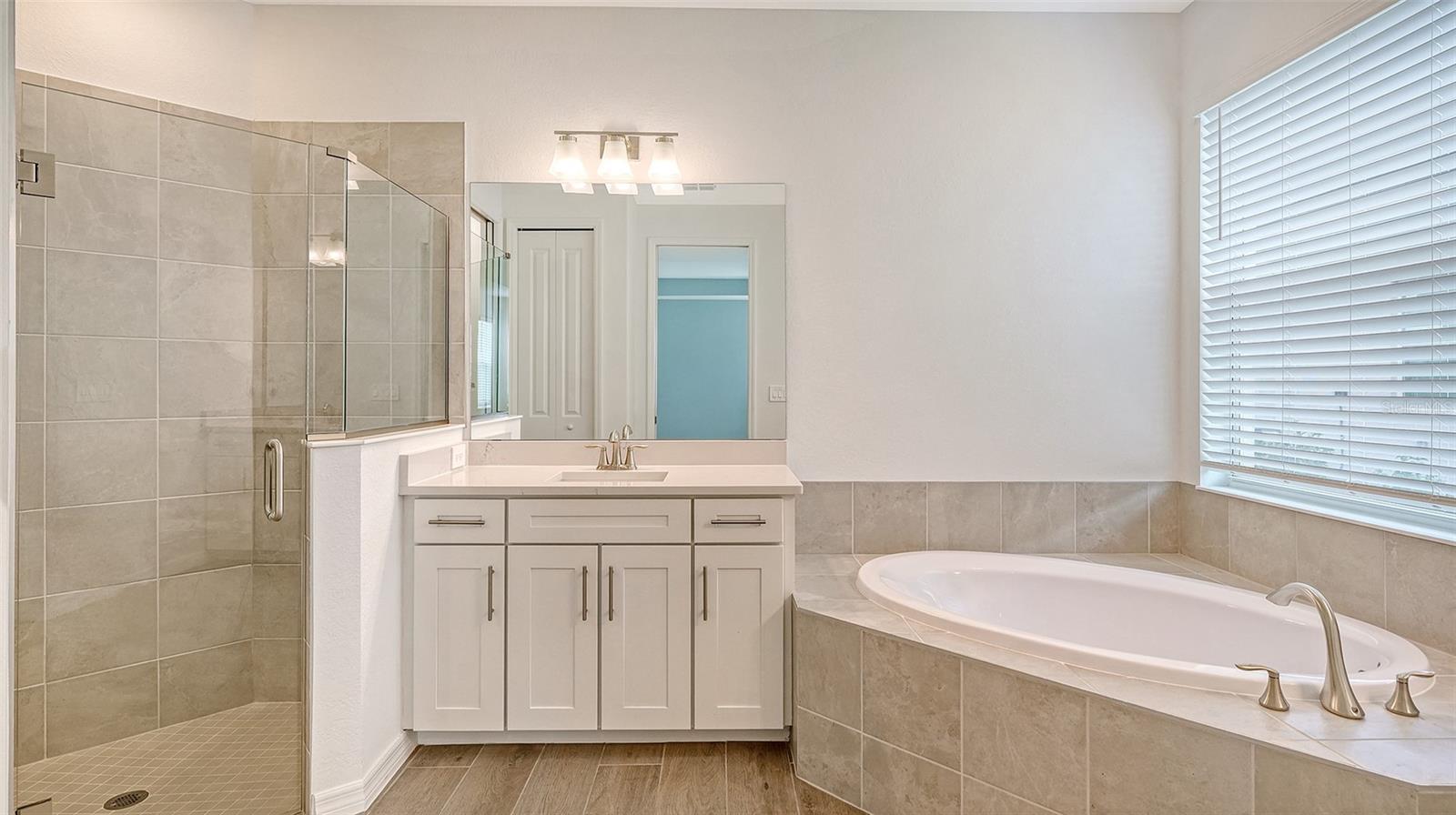 Bathroom with a glass-enclosed tiled shower, white vanity, and large oval soaking tub.