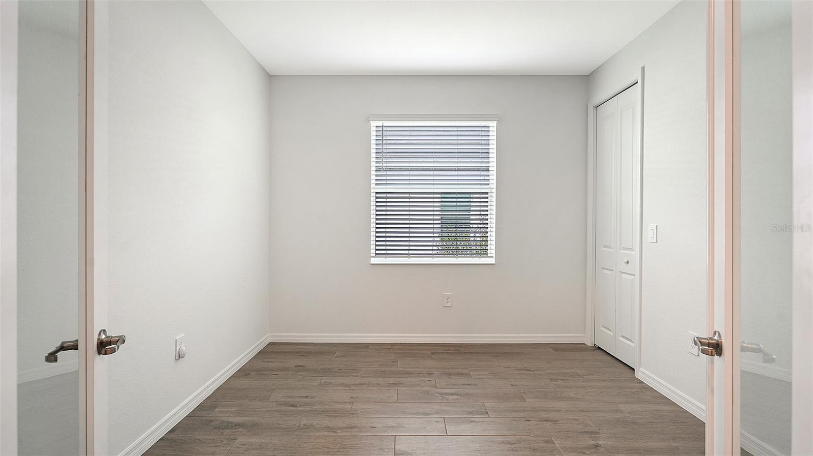 Empty bedroom with gray tile flooring, a window with blinds, and a double-door closet.