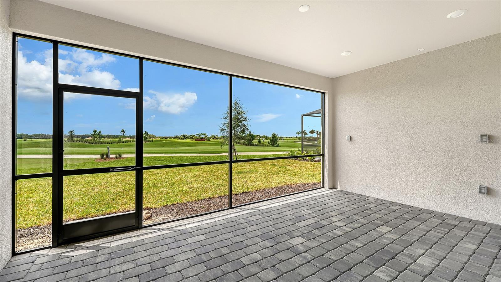 Covered patio with gray pavers and expansive windows overlooking a golf course.