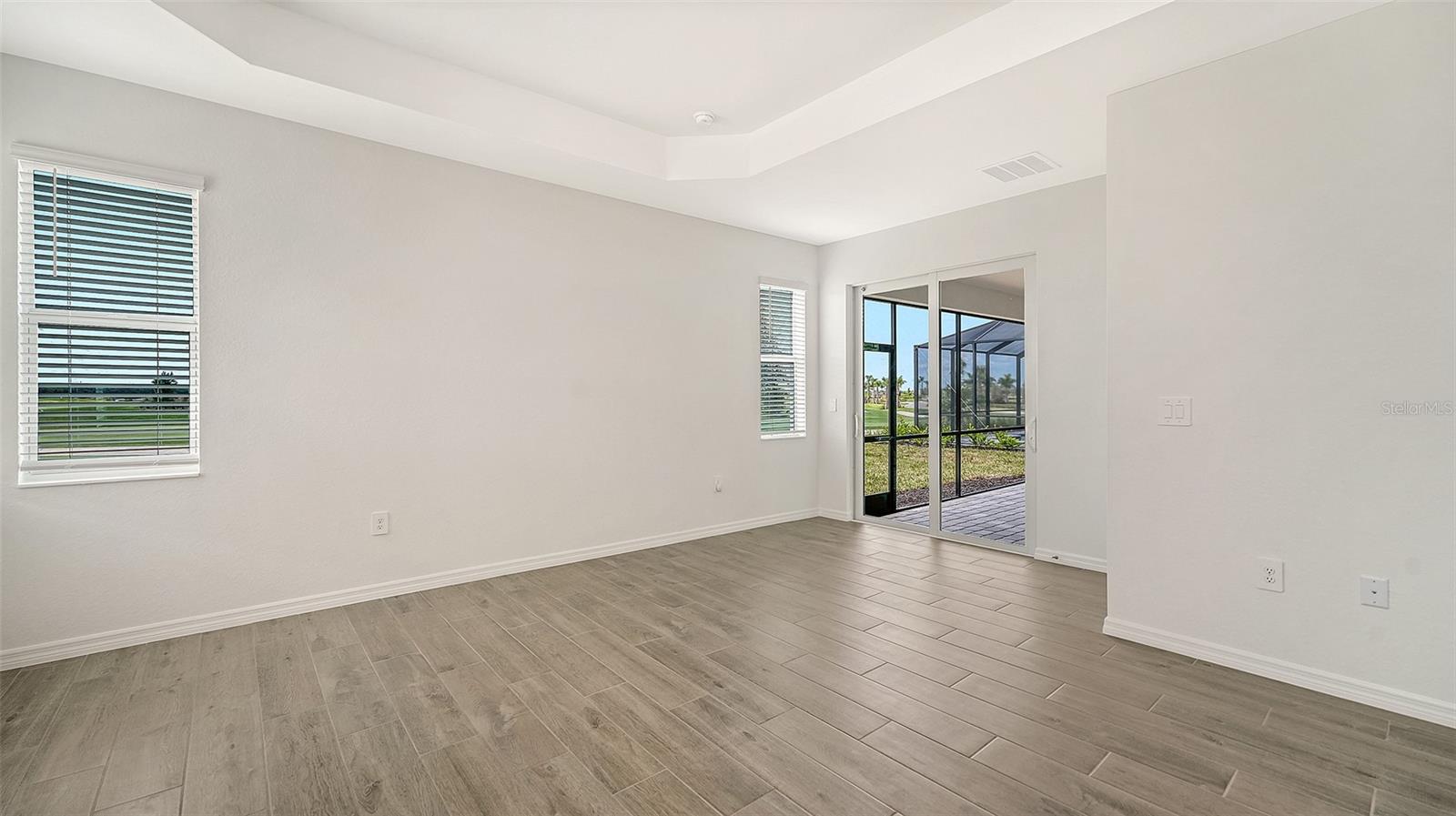 Empty room with gray wood-look tile flooring, tray ceiling, and sliding doors to a screened lanai.