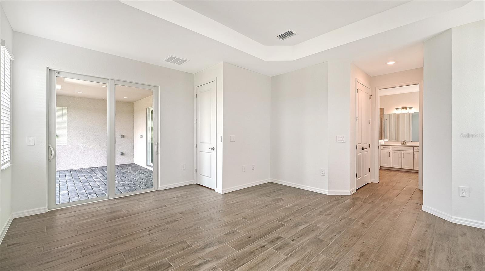 Empty bedroom with wood-look tile floors, sliding glass doors to a tiled lanai, and an adjoining bathroom.