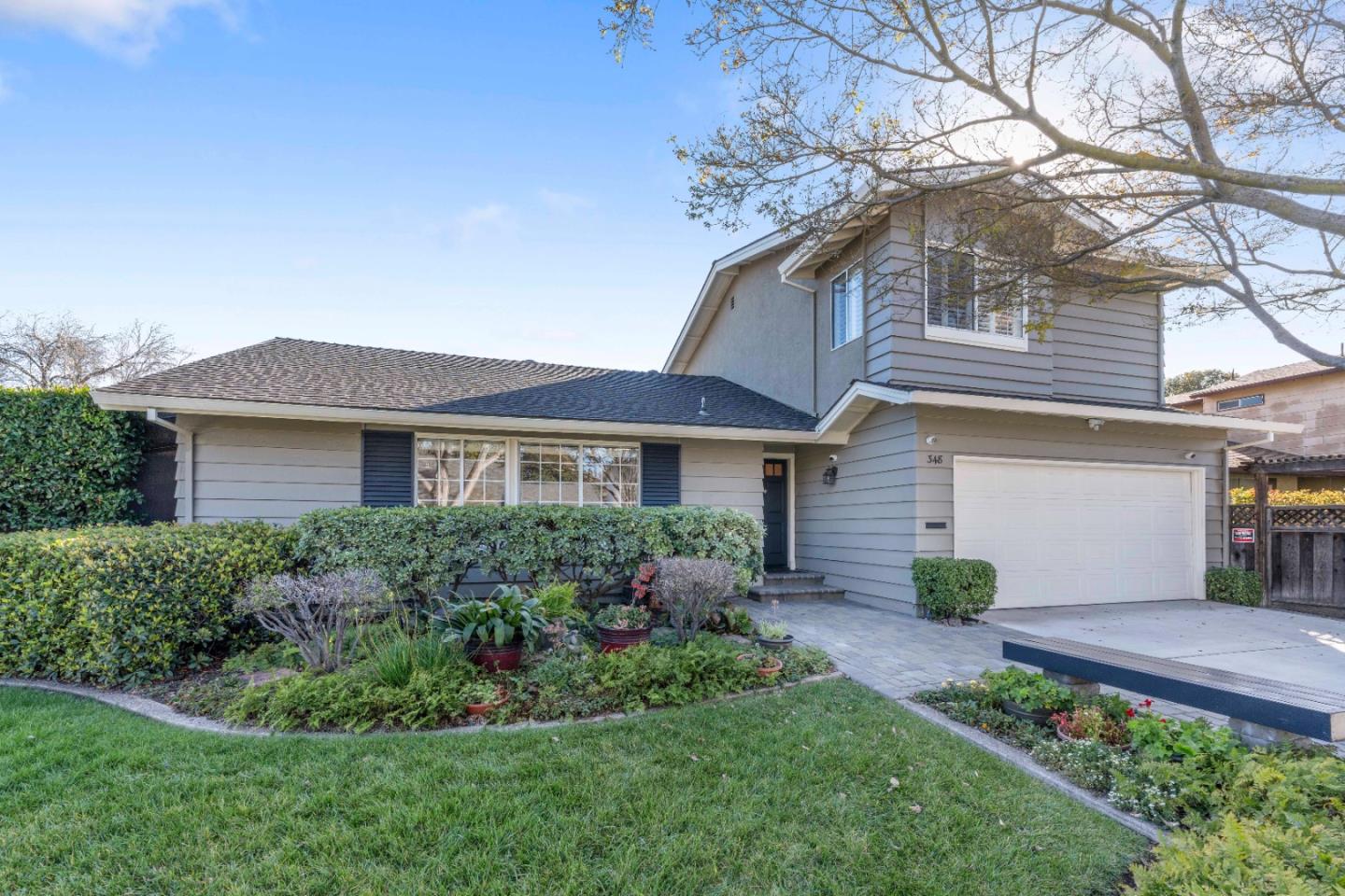 Two-story gray house with dark shutters, white garage door, and landscaped front yard.