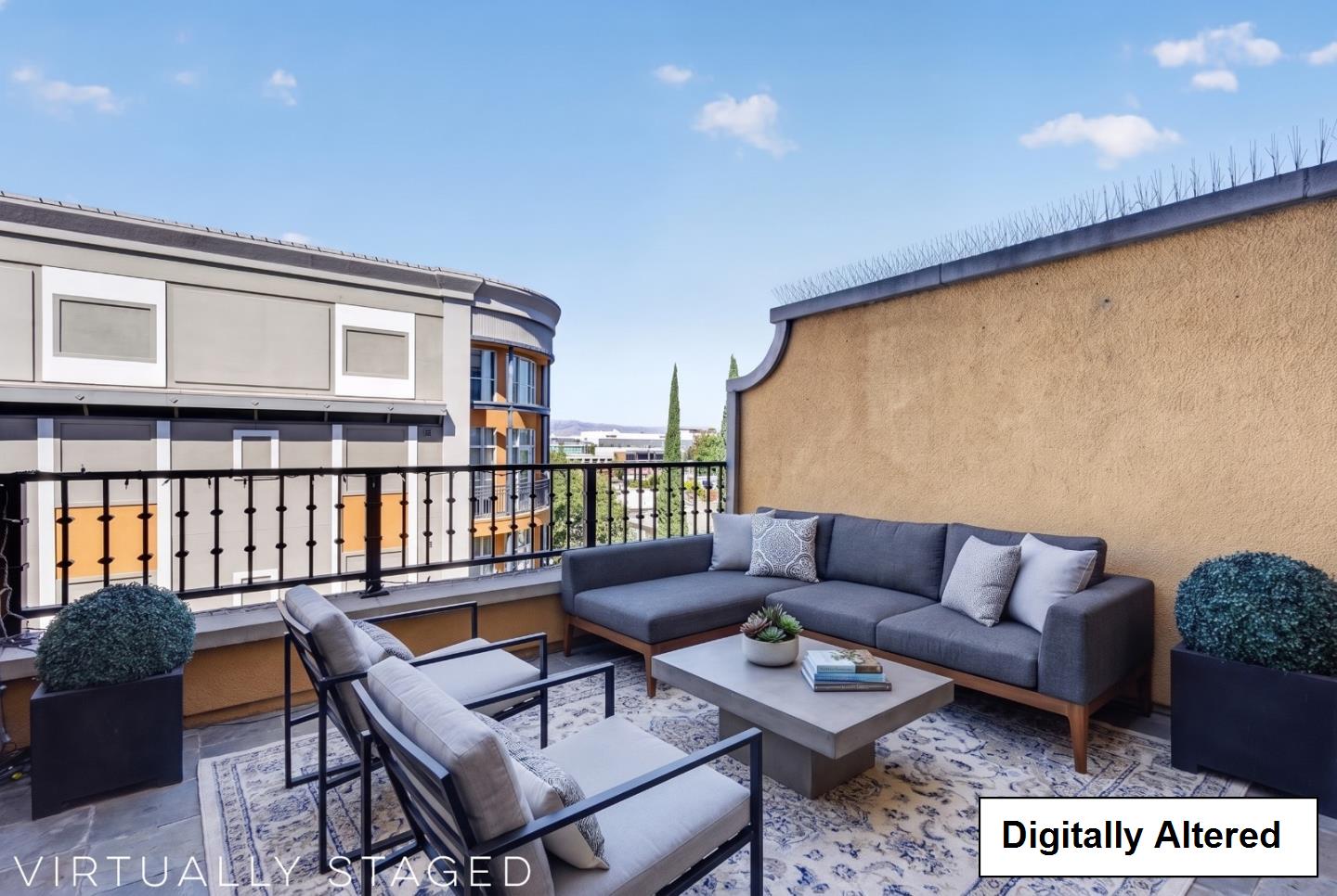Outdoor terrace with gray sectional seating, lounge chairs, a patterned rug, and potted shrubs.