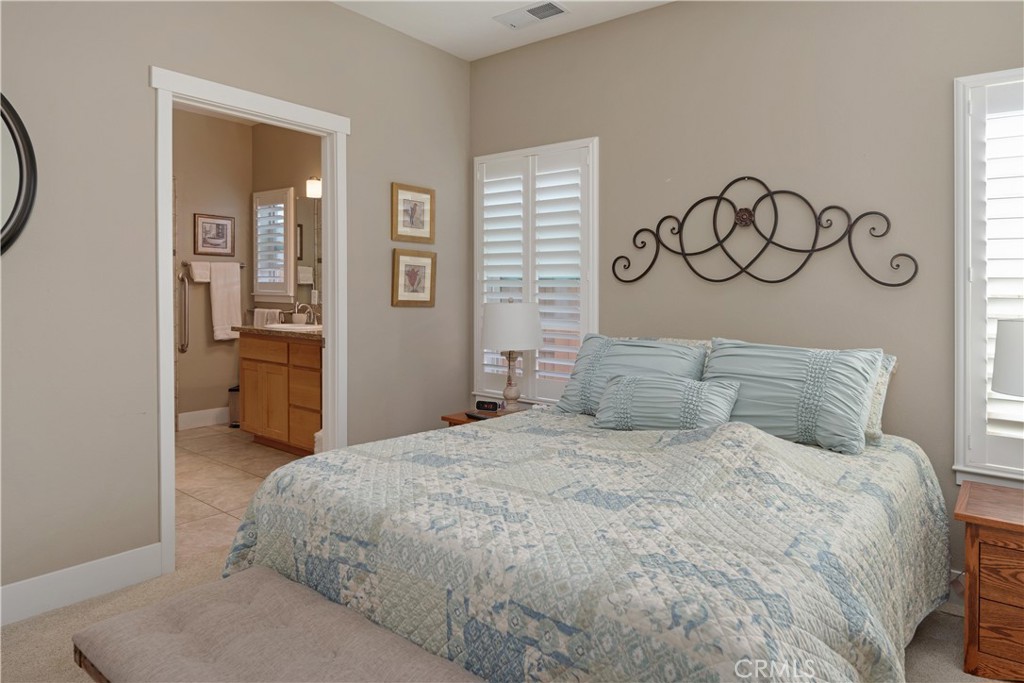 Furnished bedroom with a pale blue quilt, shuttered windows, and an ensuite bathroom doorway.