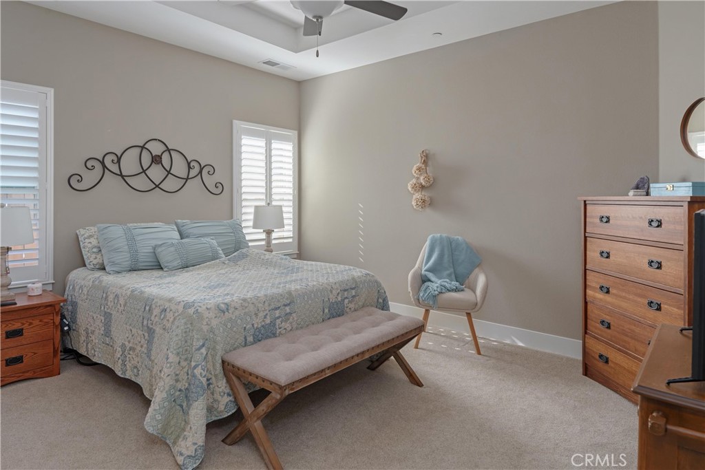 Bedroom with pale blue patterned bedding, a cushioned bench, shuttered windows, and a wooden chest of drawers.