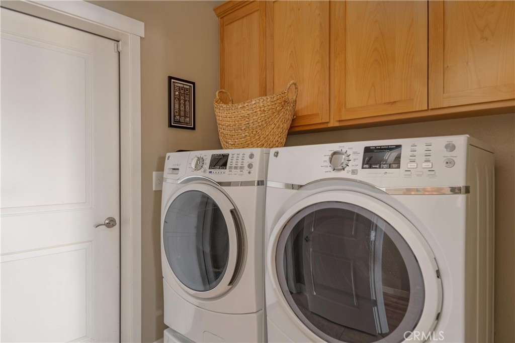 Laundry room with front-loading washer and dryer beneath wooden cabinets.