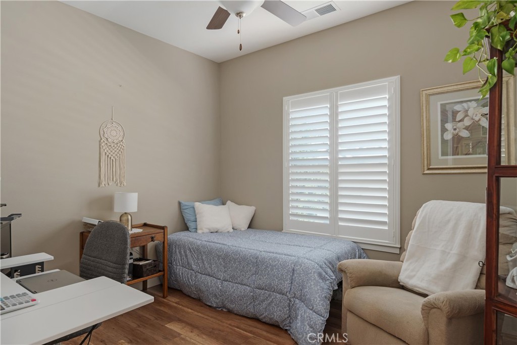 Bedroom with a single bed beneath white plantation shutters and a desk in the foreground.