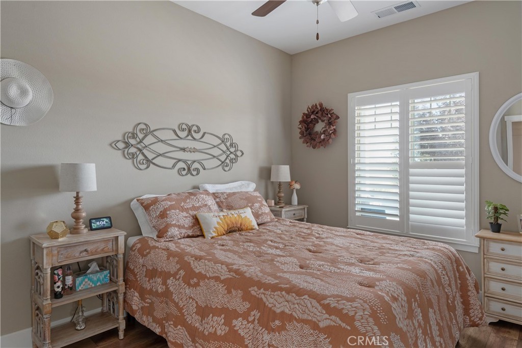 Staged bedroom with a rust-patterned bedspread and wide shuttered window.