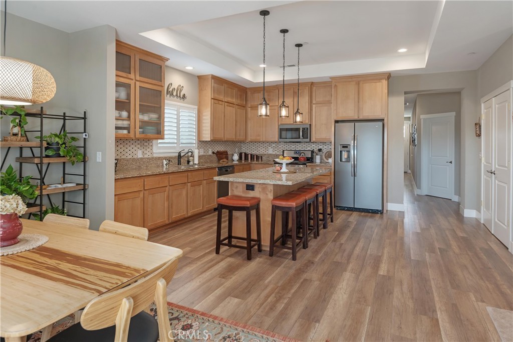 Kitchen with light wood cabinetry, granite counters, stainless appliances, and a central island with bar stools.