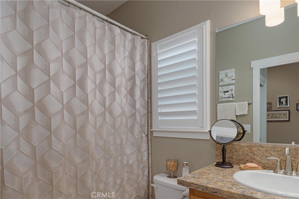 Bathroom with a geometric shower curtain, shuttered window, and granite vanity.