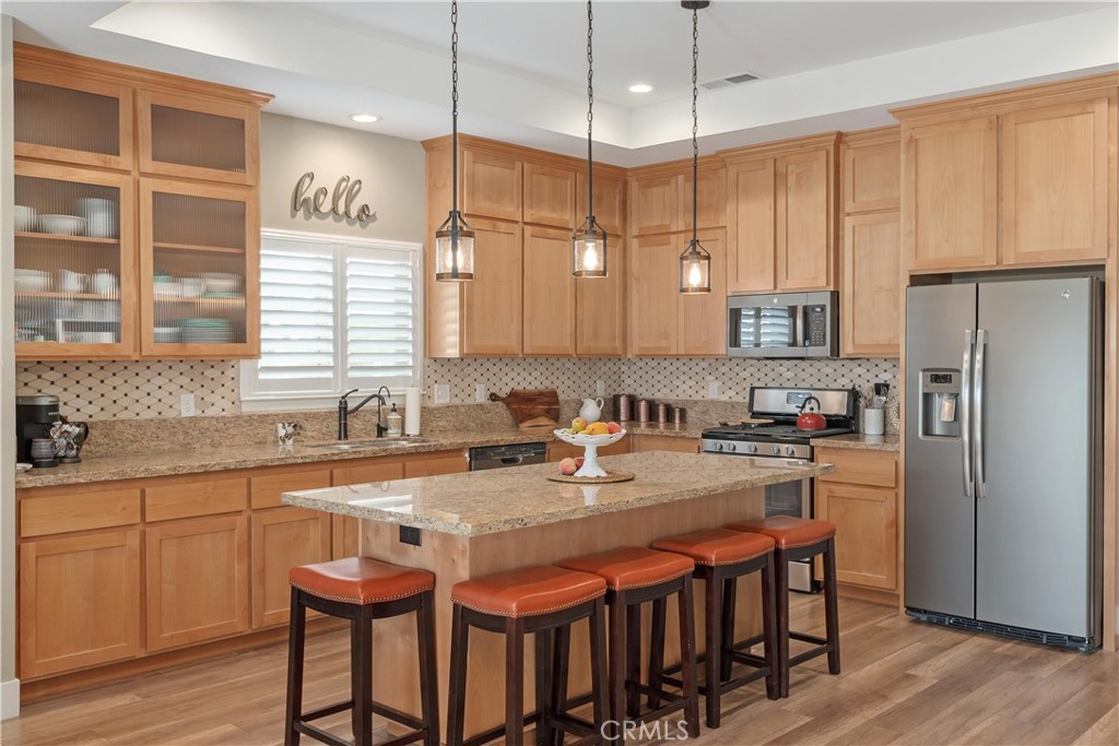 Kitchen with natural wood cabinets, granite island, stainless steel appliances, and orange-cushioned bar stools.
