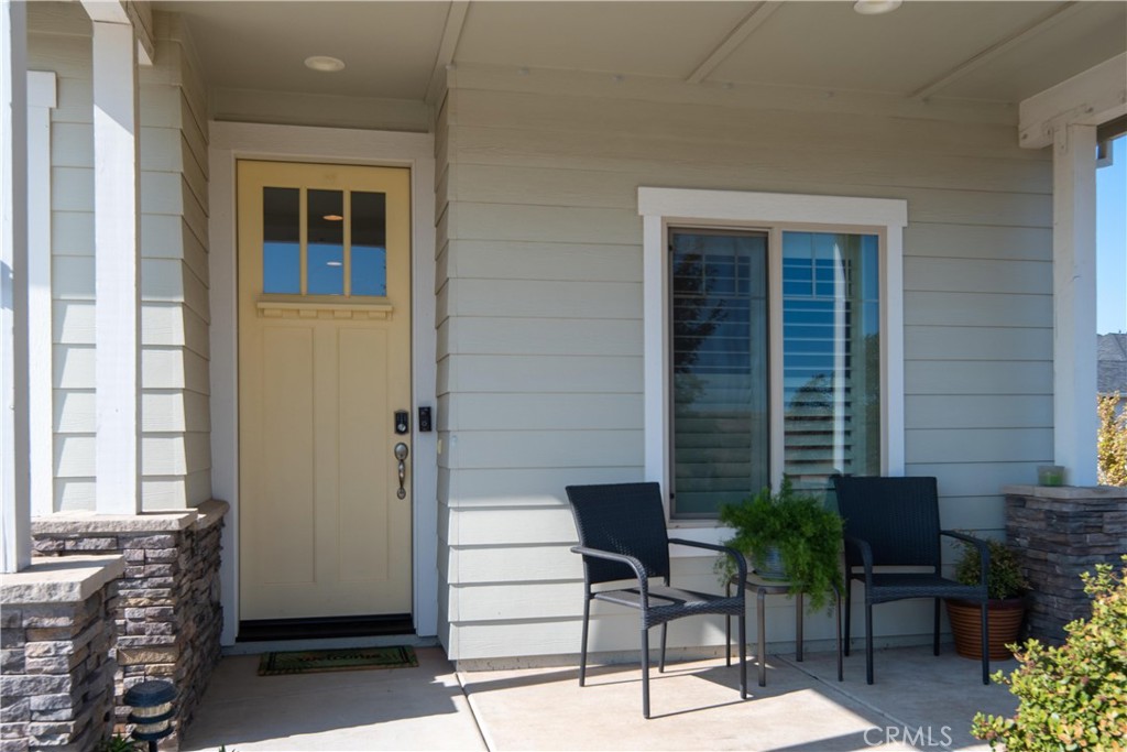 Covered front porch with a cream entry door, stone columns, and two black chairs beside a window.