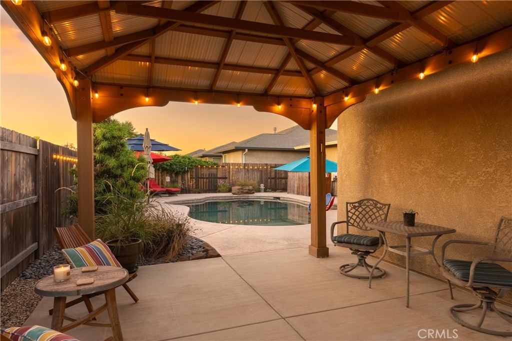 Covered patio with timber beams and string lights overlooking a fenced swimming pool.