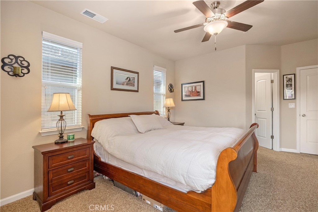 Furnished bedroom with a large wooden bed, matching nightstand, two windows, and a ceiling fan.