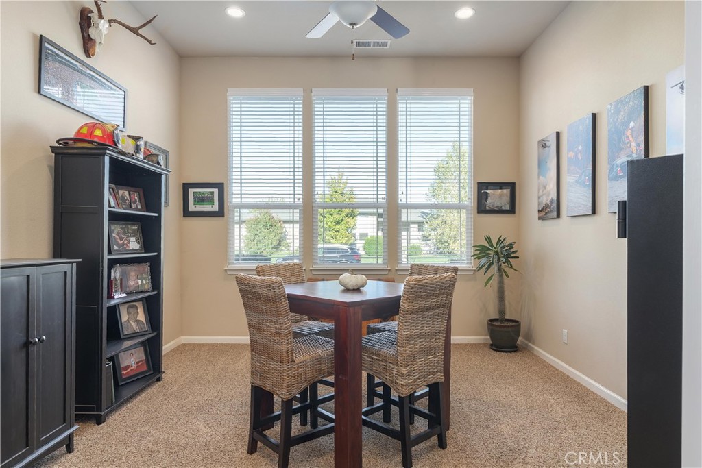 Dining area with a dark wood table, woven chairs, and three large windows with blinds.