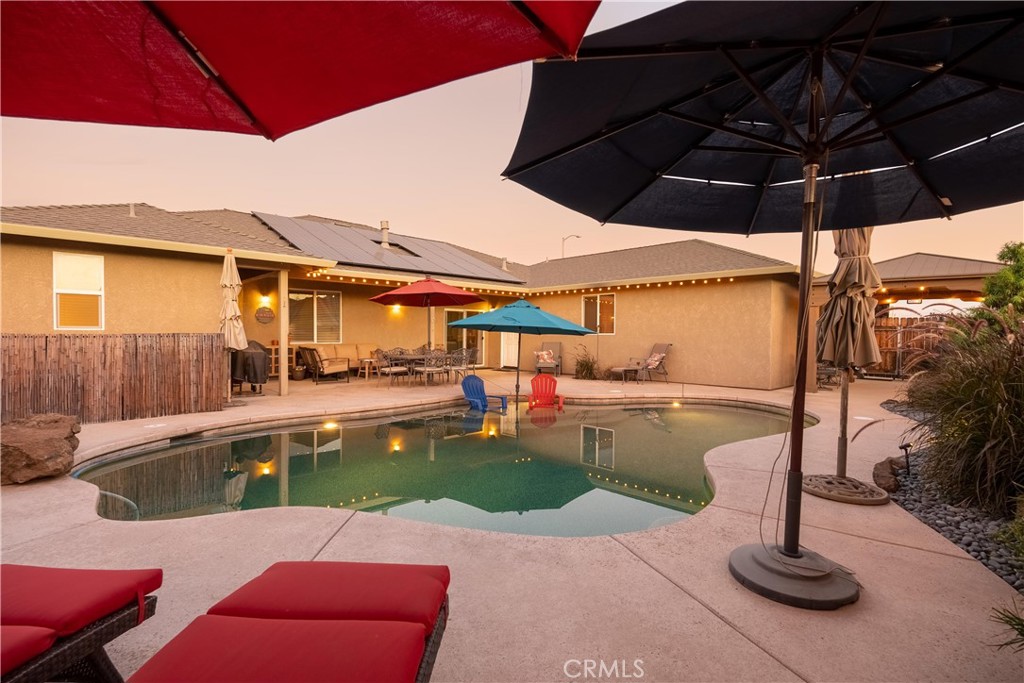 Backyard swimming pool with patio seating and umbrellas at dusk.