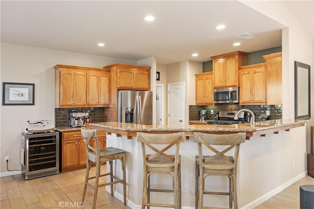 Kitchen with wood cabinetry, granite island, stainless appliances, and bar stools.