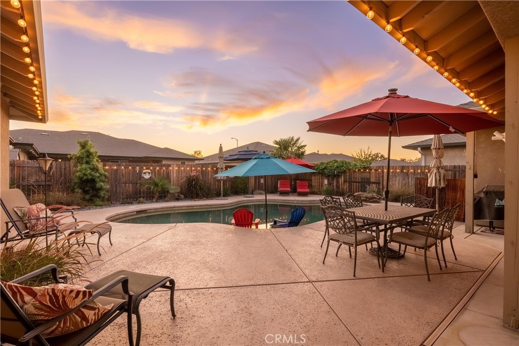 Backyard pool and furnished patio with colorful umbrellas at sunset.