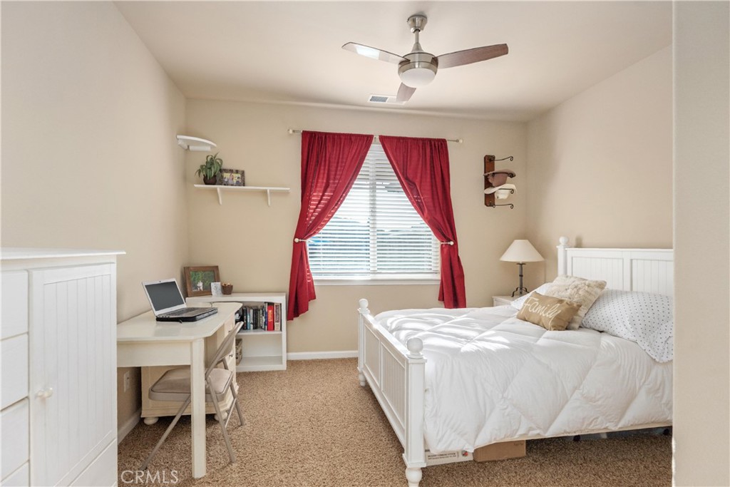 Bedroom with a white bed, desk and laptop, and red curtains framing the window.