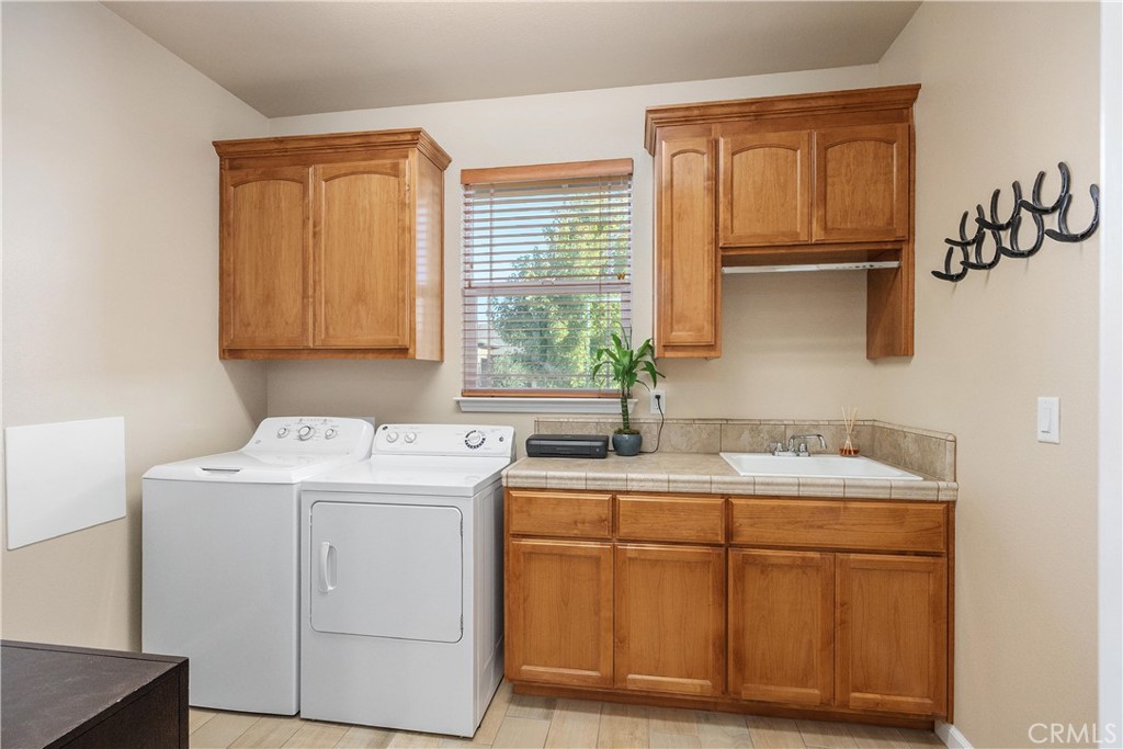 Laundry room with white washer and dryer, utility sink, and warm wood cabinetry.