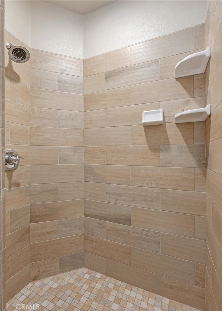 Walk-in shower with beige tile, mosaic flooring, and three built-in shelves.