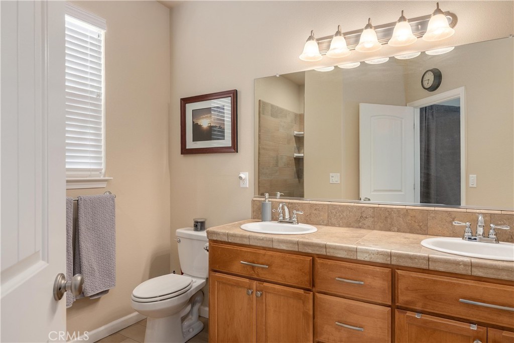 Bathroom with a double-sink vanity, warm wood cabinetry, large mirror, and toilet.