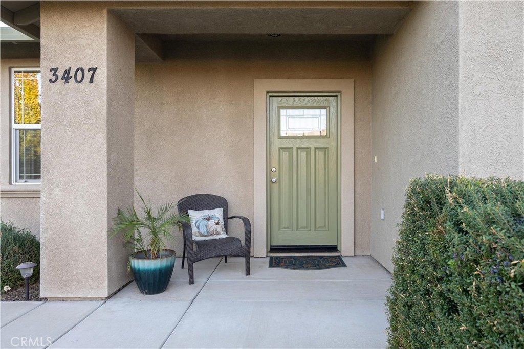 Covered front entry with a sage-green door, wicker chair, potted palm, and house number 3407.