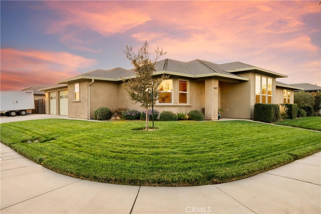 Single-story stucco home with an attached garage and broad lawn beneath a pink dusk sky.