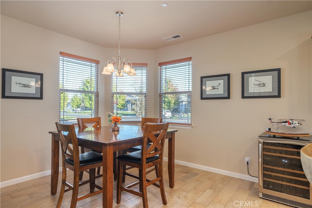 Furnished dining room with a dark wood table, chandelier, three windows, and a glass-front wine refrigerator.